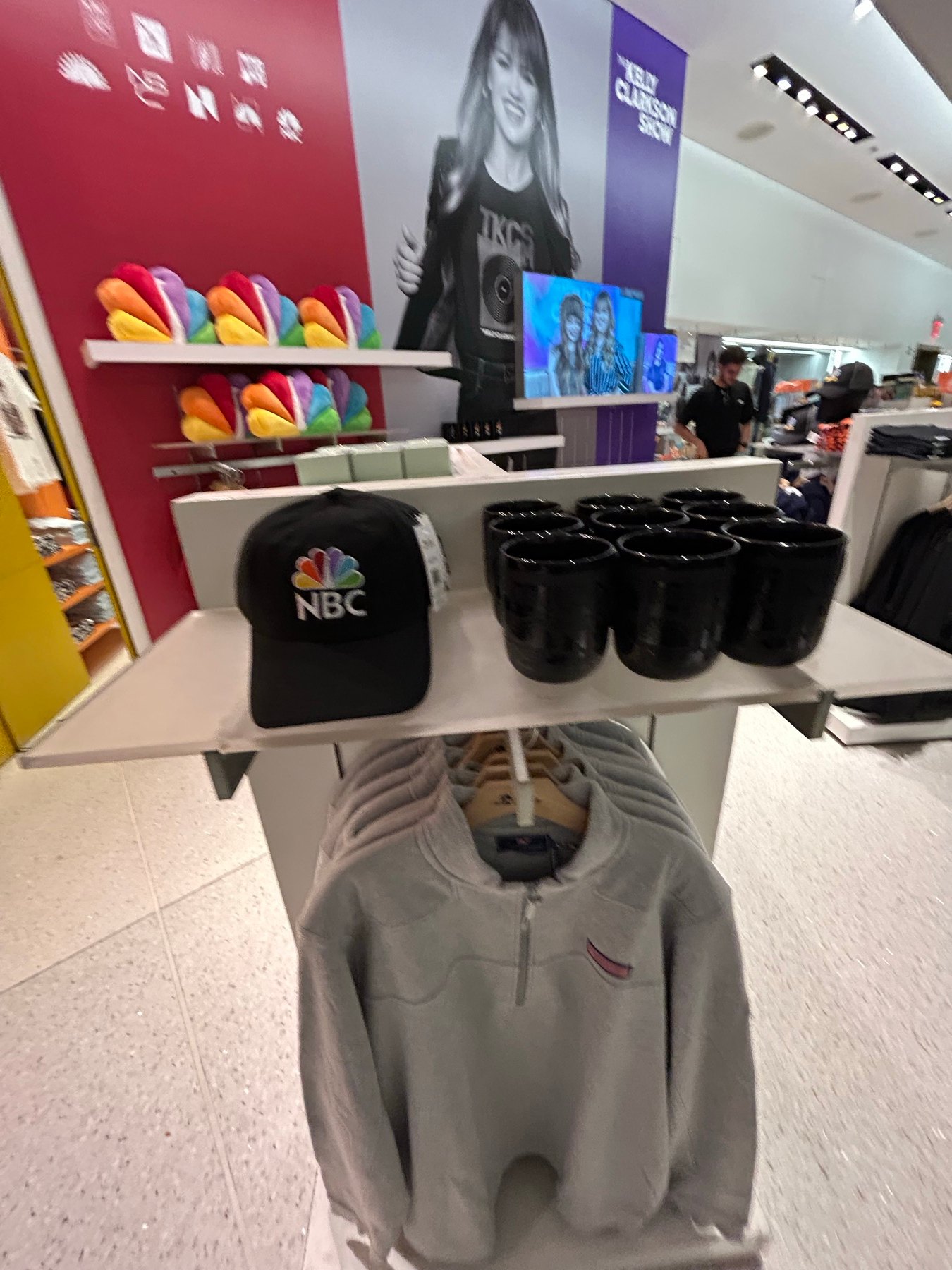 NBCロゴ入り黒キャップと番組Tシャツが並ぶ店内棚