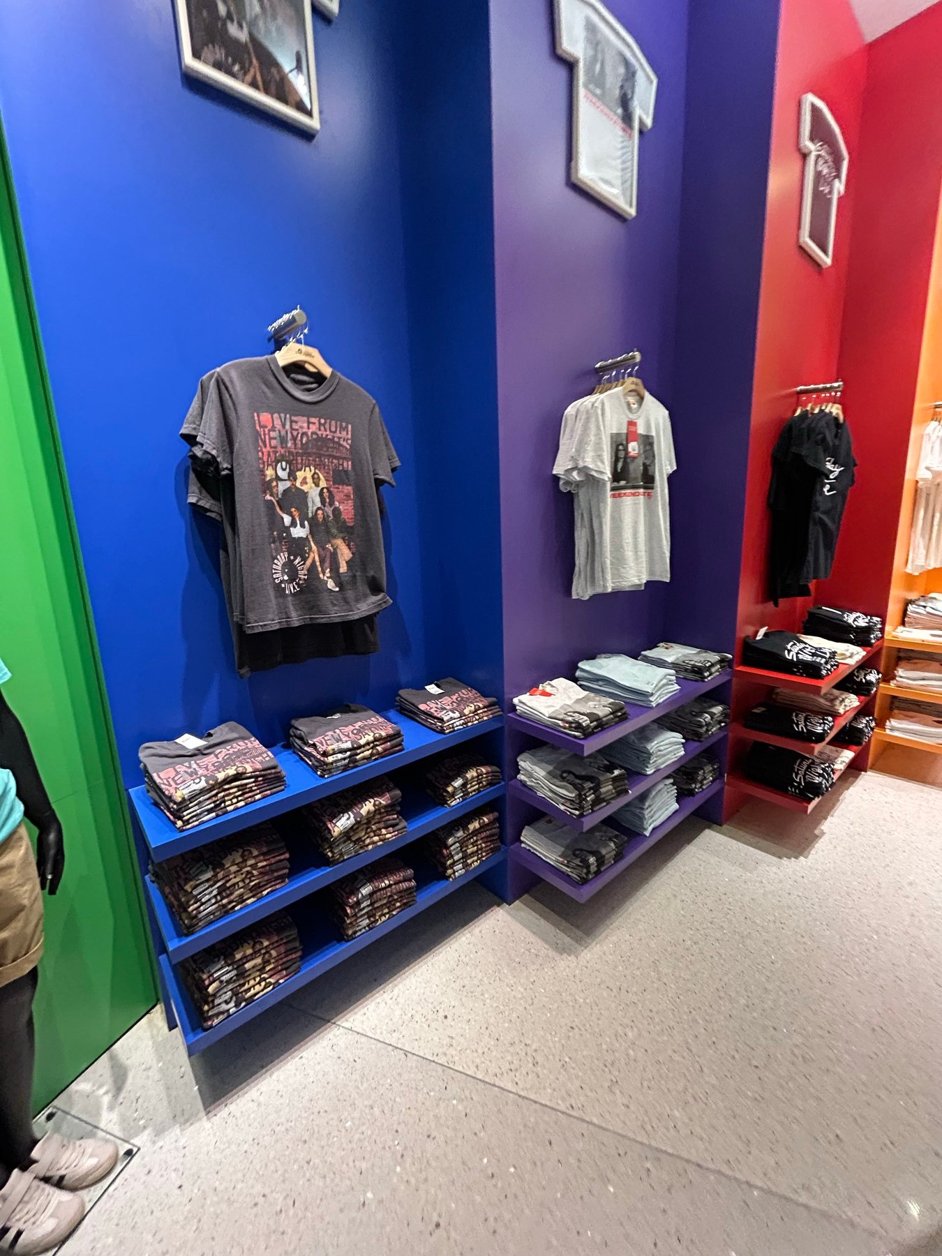 The Tonight ShowやSaturday Night Liveなどの番組Tシャツが並ぶカラフルな壁面
